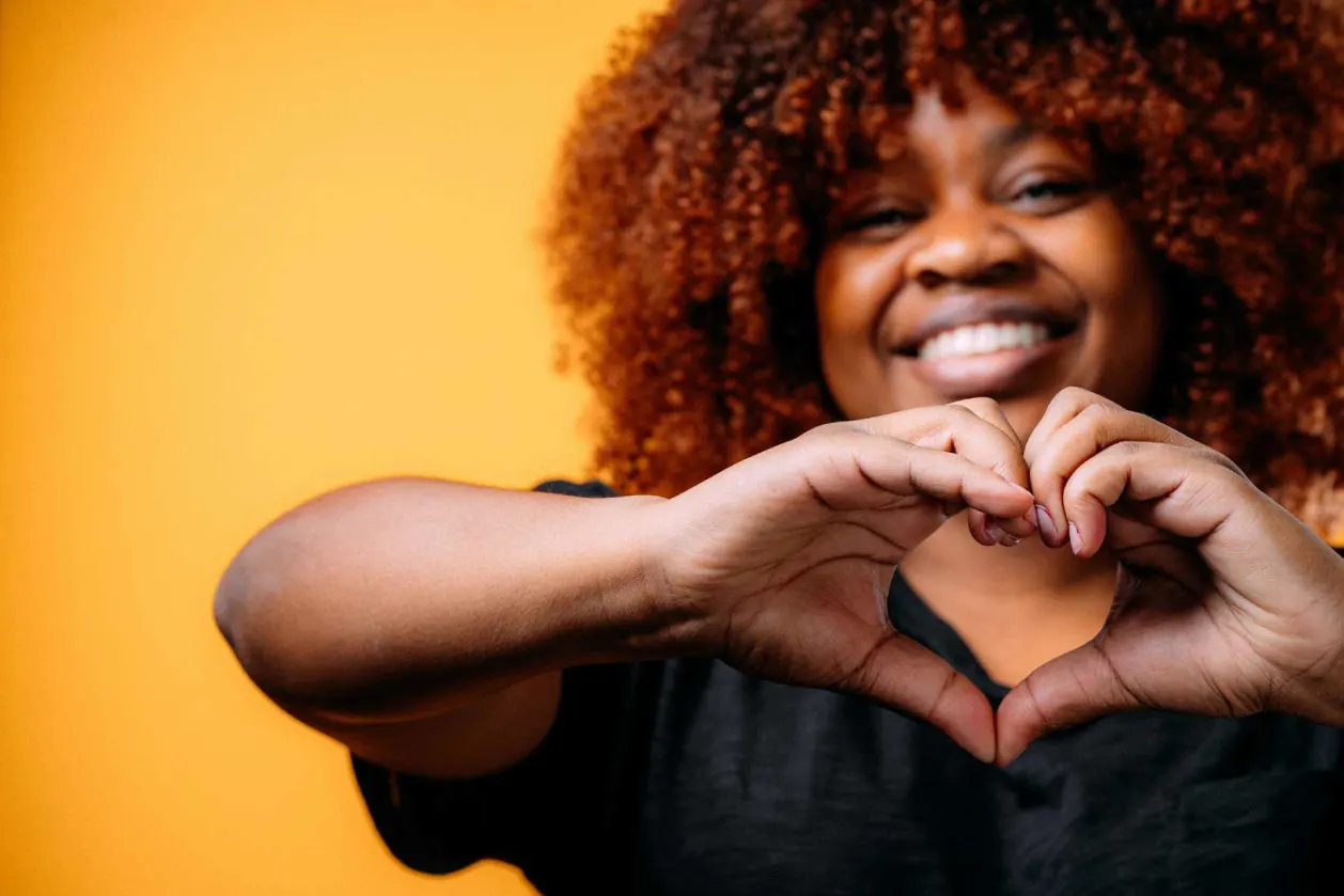 happy woman of color making a heart shape with hands